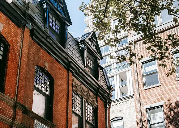 Ljust öppet kontorslandskap med stora fönster, växter och två personer som arbetar vid ett delat bord.